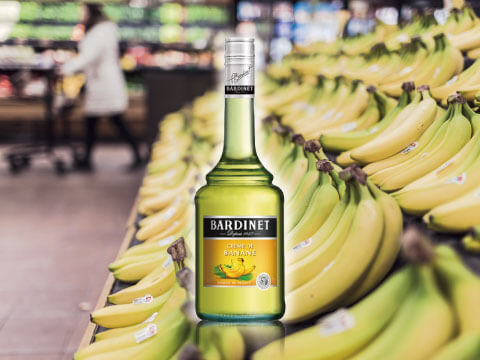 スーパーのバナナコーナーを背景にしたバナナリキュールのボトル