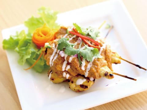 ピーナッツソースをかけた鶏の串焼き（チキンサテ）、パクチーを添えてサラダと一緒に盛り付けた様子