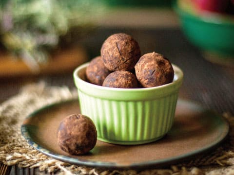 緑色の陶器のボウルに盛られたココアパウダーまぶしのチョコレートトリュフ、皿の上に一粒添えて