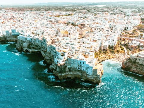 イタリア・アドリア海沿いの断崖に建つ白い街並みを空から撮影した写真。ターコイズブルーの海が広がる