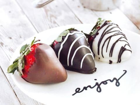 「enjoy」の文字が入った白いお皿に並ぶ、ミルク・ダーク・ホワイトの3種のチョコレートでコーティングしたいちご