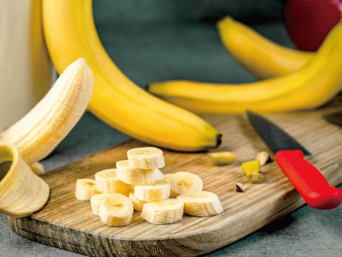まな板の上にあるカットされたバナナと皮をむく前のバナナ